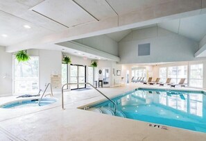 An indoor swimming pool with a 3 FT depth marker, lounge chairs, and potted plants.