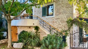 Una casa de piedra con puerta de madera, una escalera con barandilla de metal y un balcón.