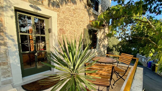 Edificio de piedra con un patio que incluye una mesa y sillas de madera, una planta en maceta y un muro de piedra.
