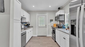 A modern kitchen with white cabinets, a stainless steel refrigerator, a microwave, and a stove. - Modern Comfort, Pet Friendly, 2 King Beds (Winter Haven)