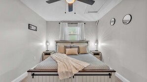 A bedroom with a bed, bedside lamps, a ceiling fan, and a window with curtains. - Modern Comfort, Pet Friendly, 2 King Beds (Winter Haven)