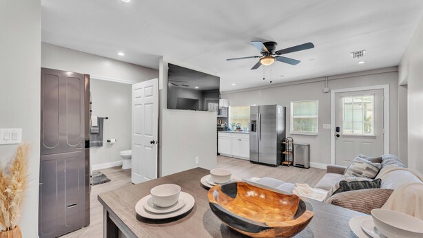 A modern kitchen with stainless steel appliances, a dining area with a wooden bowl centerpiece, and a living room with a sofa and cushions. - Modern Comfort, Pet Friendly, 2 King Beds (Winter Haven)