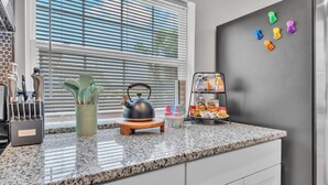 A kitchen with granite countertops, a kettle, a utensil holder, a drink dispenser, and a refrigerator with magnets. - Modern Comfort, Pet Friendly, 2 King Beds (Winter Haven)