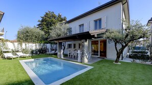 Een modern huis met een zwembad, een overdekt terras en een verzorgd gazon.