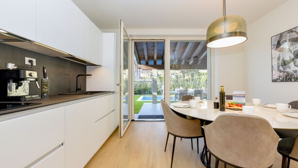 Een moderne keuken met witte kasten, een ingebouwde espressomachine en een eethoek met een tafel en stoelen.