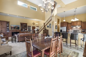 Uma sala de estar ampla com lareira, uma mesa de jantar com cadeiras, uma cozinha equipada com eletrodomésticos modernos e uma escada que dá para um andar superior.