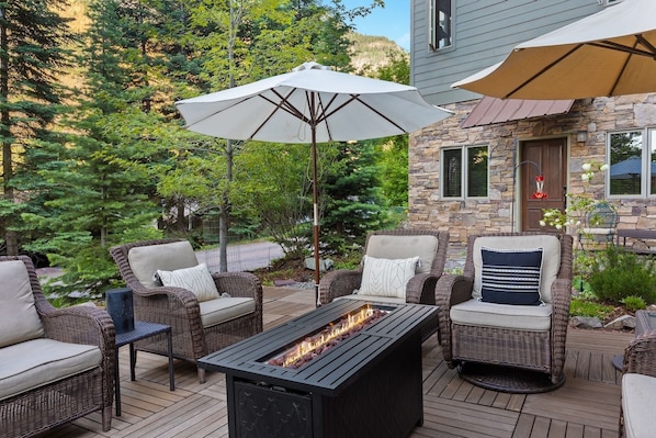A patio with wicker furniture, a fire pit, and two umbrellas. - Spacious Retreat | Incredible Views & Outdoor Space | Close to Town (Ouray)