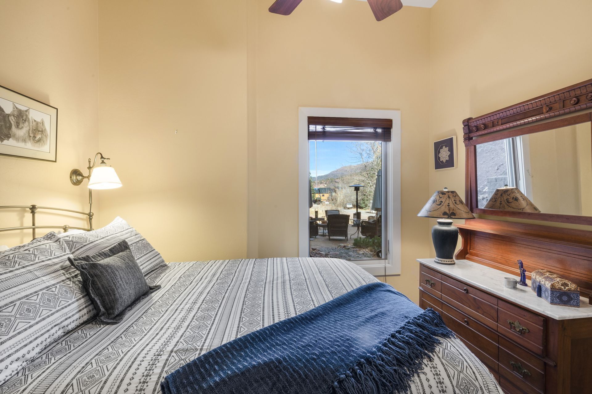 A bedroom with a bed, a dresser, a lamp, and a door leading to an outdoor area.