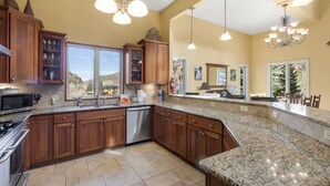 A spacious kitchen with granite countertops, wooden cabinets, stainless steel appliances, and large windows offering a view of the outdoors. - Spacious Retreat | Incredible Views & Outdoor Space | Close to Town (Ouray)