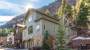 A two-story house with a stone foundation and a gabled roof, surrounded by trees and a mountain backdrop. - Spacious Retreat | Incredible Views & Outdoor Space | Close to Town (Ouray)