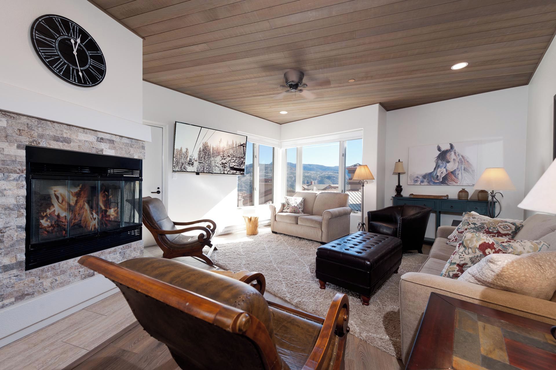 A spacious living room with a fireplace, comfortable seating, and large windows offering a view of the outdoors.
