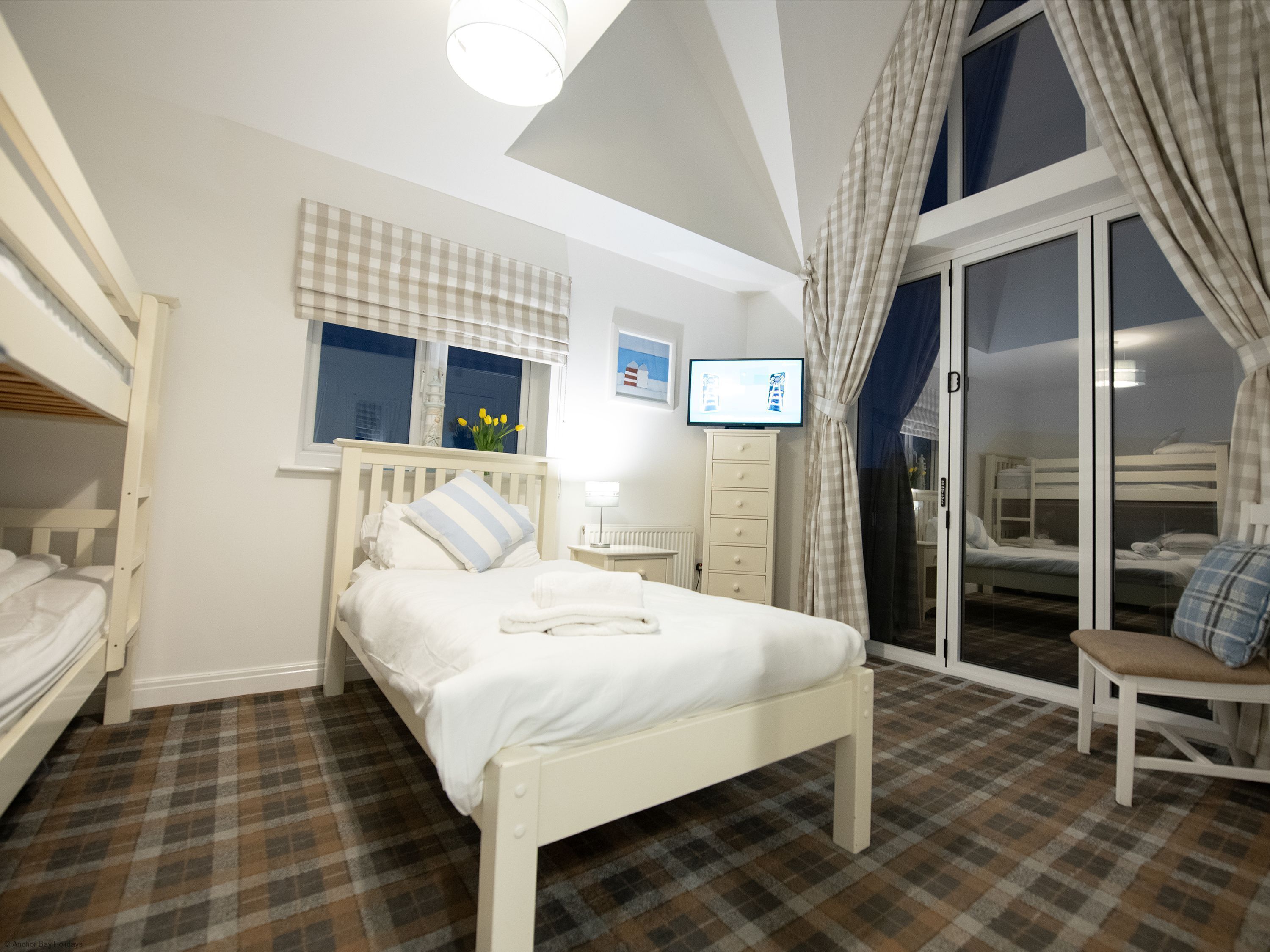 A bedroom with a bed, a TV, a window with curtains, a radiator, and a checkered floor.