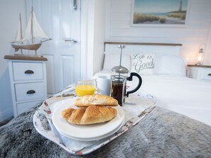 Ett brickbord med croissanter, ett glas apelsinjuice och en kaffepress på sängen.