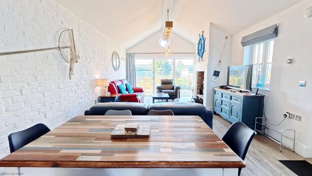 A modern living room with a wooden dining table, a red sofa, and a television. - Stunning Beach House - Sleeping 6 in 3 Bedrooms - Pool and Beach Access Included. (Filey)