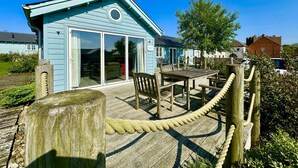 A light blue building with a large sliding glass door, wooden deck, and rope barrier. - Stunning Beach House - Sleeping 6 in 3 Bedrooms - Pool and Beach Access Included. (Filey)