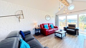 A modern living room with a white brick wall, leather sofas, a red leather couch, a black leather armchair, and a wooden coffee table. - Stunning Beach House - Sleeping 6 in 3 Bedrooms - Pool and Beach Access Included. (Filey)