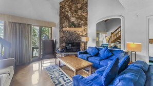 A spacious living room with a stone fireplace, blue leather sofa, and a wooden coffee table. - Cm425 Copper Mtn Inn 5 Bedroom Condo by RedAwning (Copper Mountain)