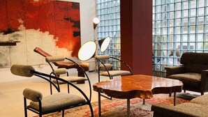 Ein modernes Interieur mit einem großen Fenster, einem roten abstrakten Gemälde und einer Mischung aus Metall- und Polstermöbeln.
