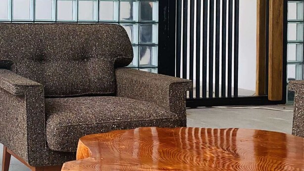 Ein modernes Interieur mit einem gemusterten Sofa, einem Holztisch und einer Glastrennwand mit vertikalen Jalousien.