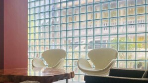 Ein modernes Interieur mit einem großen Fenster, zwei weißen Stühlen, einem dunklen Sofa und einem Holztisch.