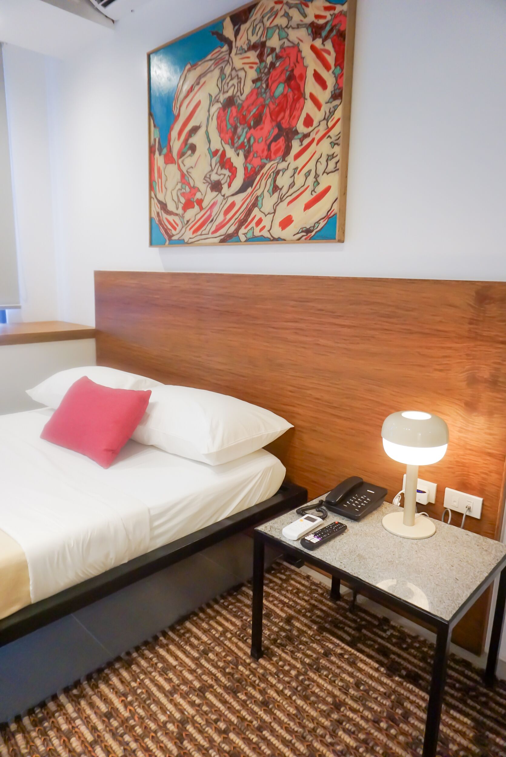 A hotel room with a bed, a nightstand, a lamp, and a painting on the wall.