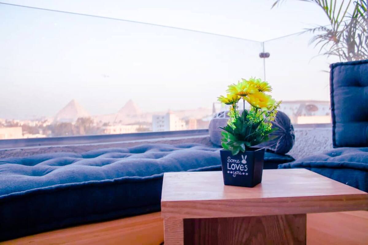 A cozy seating area with a view of pyramids, a small table with a plant, and a cushion.