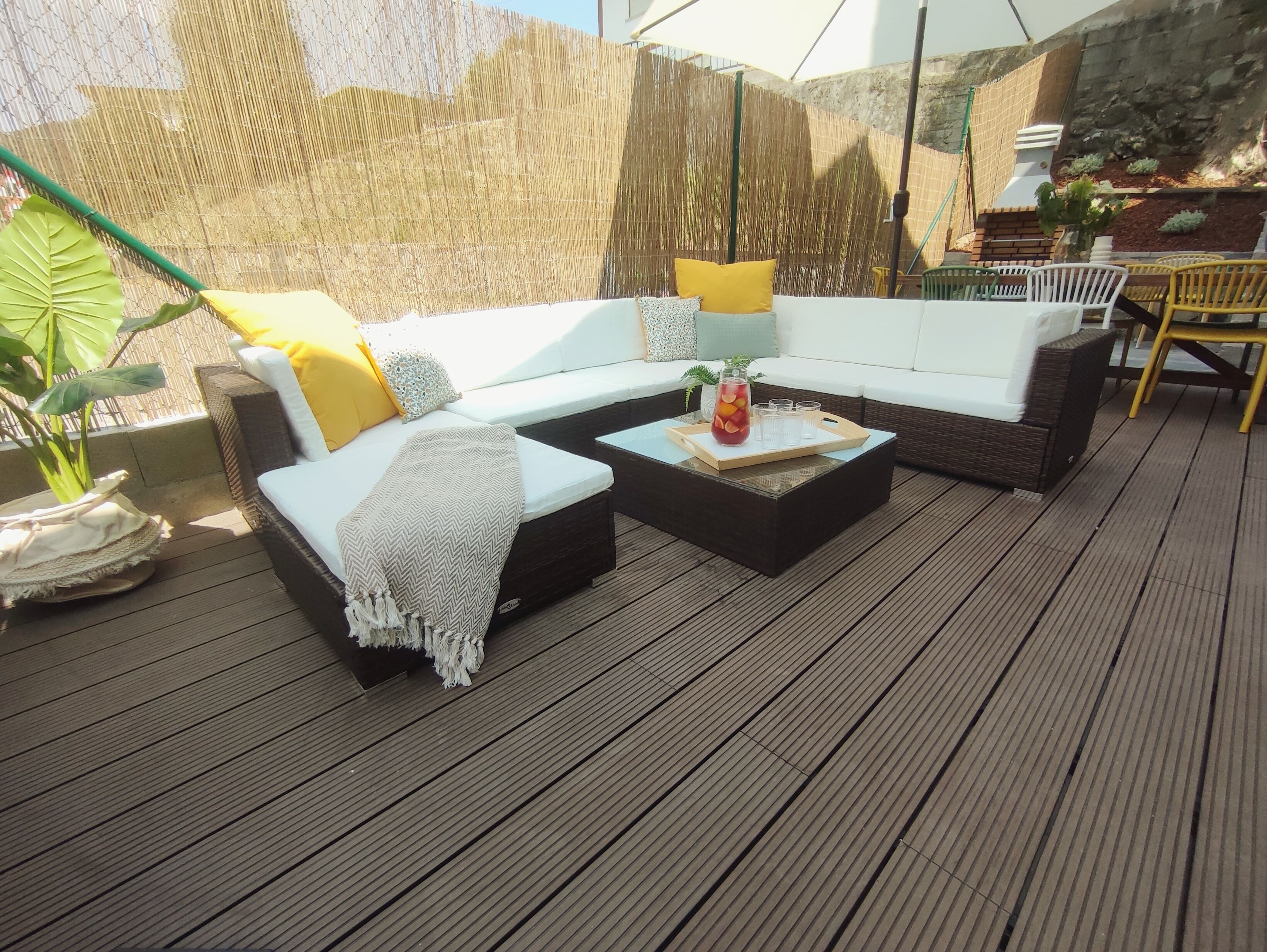 A wooden deck with a sectional sofa, a coffee table, and a potted plant.