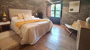 Un dormitorio rústico con una cama grande, pisos de madera, una pared de piedra y una ventana con vistas.
