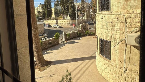 A view through a window with a stone building, a tree, and a clear sky. - Antica Jabalal-lwebdeh 5 (Amman)