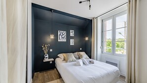 A modern bedroom with a dark wall, a large bed, a window with curtains, and wall-mounted lights. - L'azur, Cocooning, Reposant, Déposez vos Valises et Appréciez (Segré-en-Anjou Bleu)