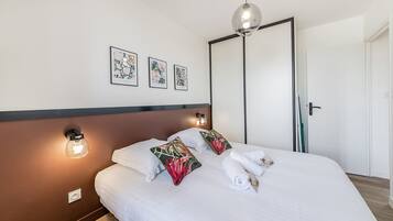 En pænt redt seng med hvide sengetæpper, to dekorative puder og en hængende lampe over.