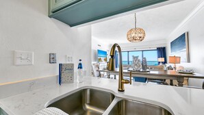 A modern kitchen with a double sink, stainless steel appliances, and a pendant light. - 🌴Emerald Towers 1302 - Salty Smile | Private Beach Access, Panoramic Gulf Views (Destin)
