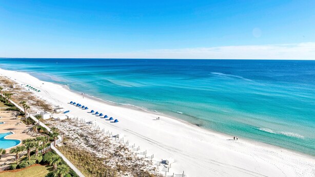 A beach resort with a long sandy beach, a pool, and several umbrellas. - 🌴Emerald Towers 1302 - Salty Smile | Private Beach Access, Panoramic Gulf Views (Destin)