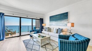 A modern living room with a balcony overlooking the sea, a white sofa, striped armchairs, and a coffee table. - 🌴Emerald Towers 1302 - Salty Smile | Private Beach Access, Panoramic Gulf Views (Destin)