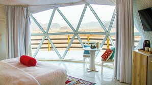 A room with a large window, a bed, a small table, and a TV. - Desert Season Camp (Wadi Rum)