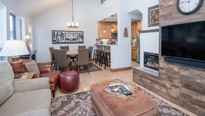 A spacious living room with a fireplace, a dining area, and a kitchen visible through an open archway.