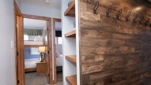 A room with a bunk bed, a bedside table with a lamp, and a wooden wall with hooks.