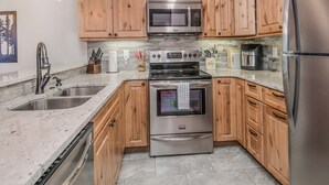 A modern kitchen with wooden cabinets, stainless steel appliances, a granite countertop, and a sink.