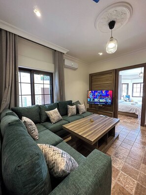 A living room with a sectional sofa, a wooden coffee table, a flat-screen TV, and a ceiling light fixture.