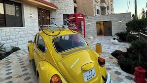 A vintage yellow car parked in front of a building with a stone facade and a red telephone booth.