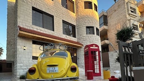 A yellow vintage car parked in front of a building with a stone facade, a red telephone booth, and a gated entrance.
