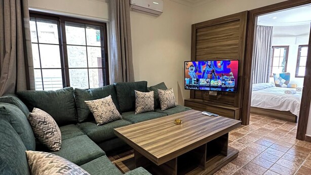 A modern living room with a sectional sofa, a wooden coffee table, a flat-screen TV, and patterned floor tiles.