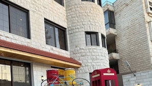 A yellow vintage car parked in front of a building with a stone facade and a red telephone booth.
