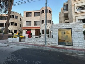 A multi-story building with a stone facade, a red telephone booth, and a sign advertising rental apartments.