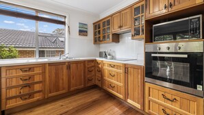Une cuisine avec des meubles en bois, un four en acier inoxydable et une fenêtre équipée de stores.