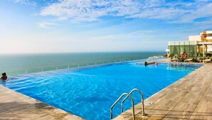 A swimming pool with a view of the ocean, a lifeguard chair, and a building with a glass facade. - Apartamento Lujoso H2 - Bocagrande (Cartagena)