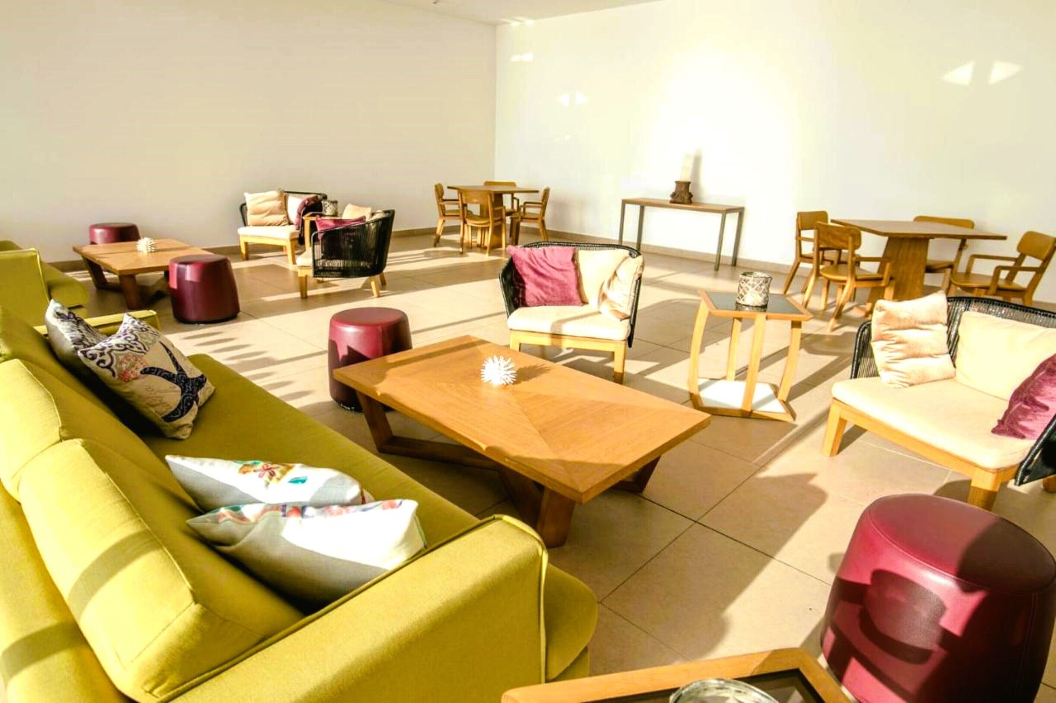 Un vaste espace de vie agrémenté d’un canapé jaune, d’une table basse en bois et de nombreux sièges, notamment des chaises et un divan.