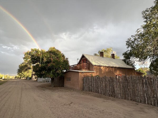 Una casa de campo con un camino de tierra, una valla de madera y un árbol.