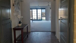 Un couloir au sol en bois, une petite table avec un vase, et une porte sur la droite.