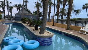 A swimming pool with blue tiles, palm trees, and inflatable rings. - Oceanfront King Suite - Fabulous Views - King Bed - Indoor and Outdoor pools (Myrtle Beach)